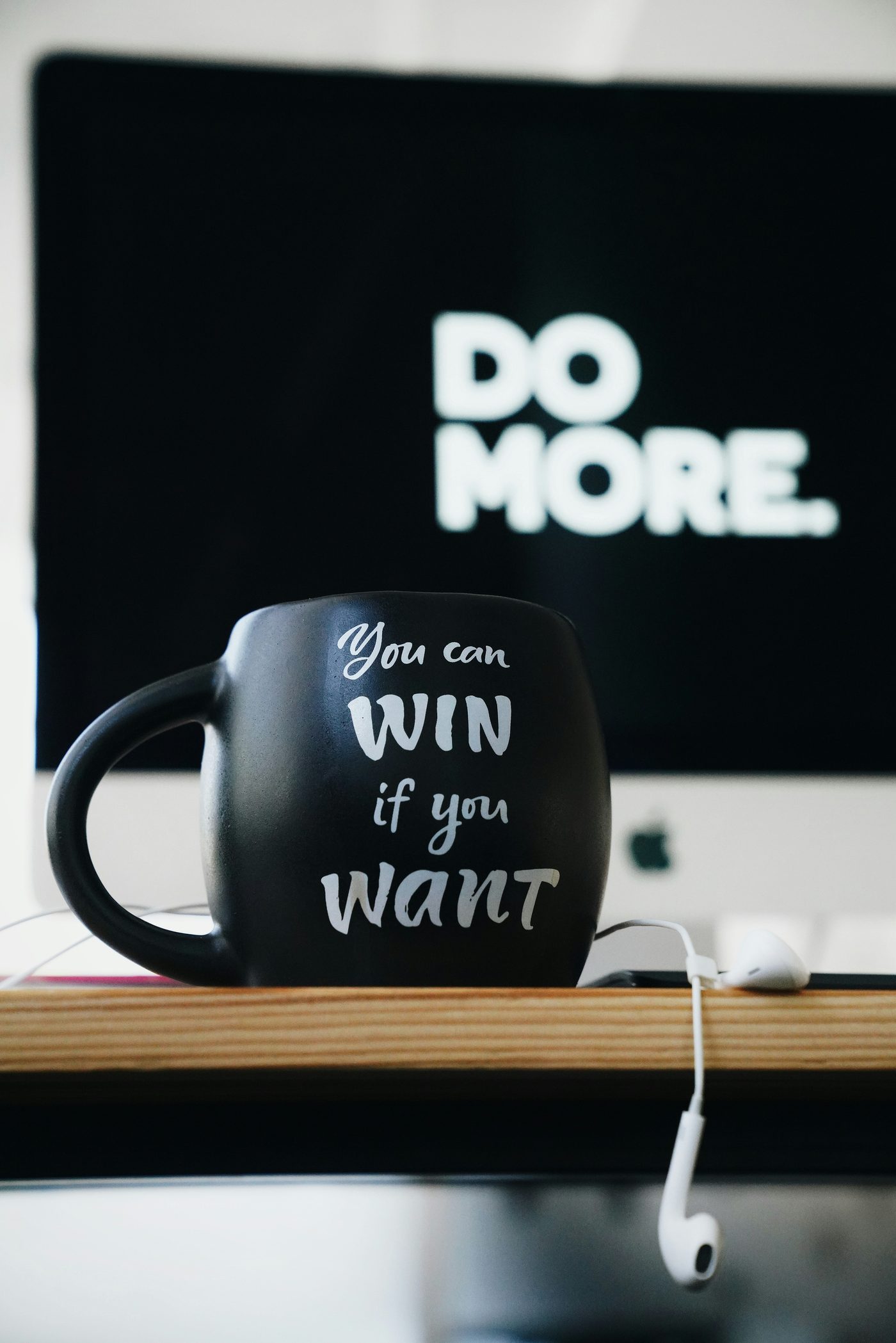 Eine schwarze Tasse mit der Aufschrift „You can win if you want“ vor einem Bildschirm mit der Aufschrift „Do more.“